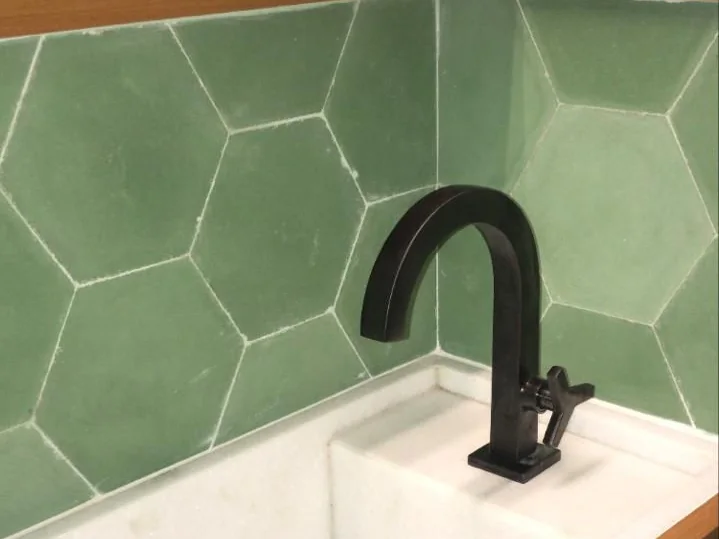 Lavabo com revestimento hexagonal verde, cuba esculpida e metais pretos