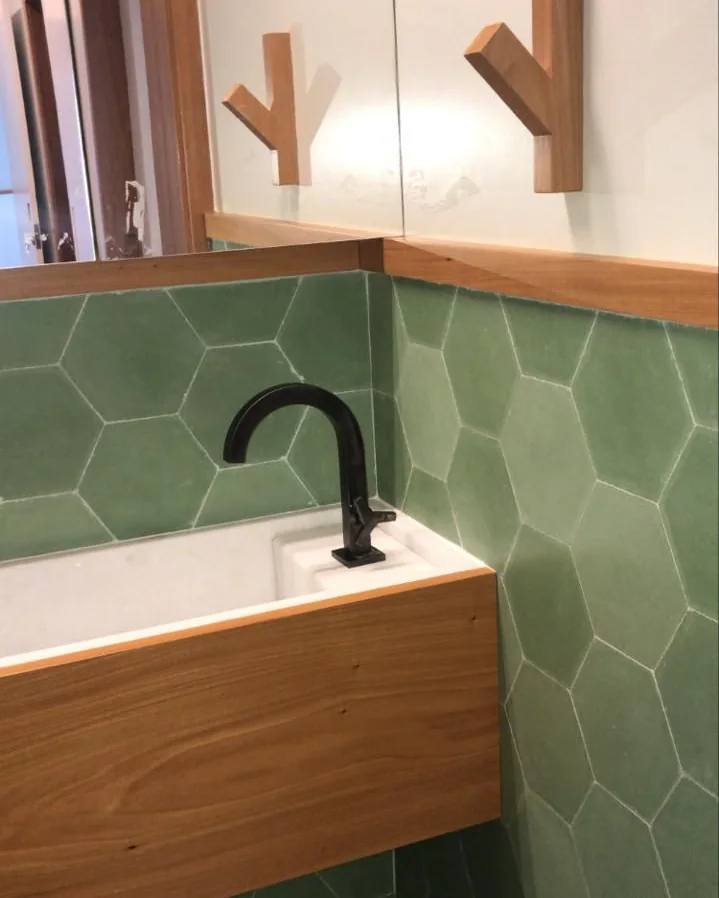 Lavabo com revestimento hexagonal verde, cuba esculpida e marcenaria em madeira